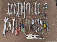 Complete view of tool lot showing array of hand tools laid out on brown cloth including combination wrenches, adjustable wrenches, pliers, screwdrivers, socket pieces and bit holder.
