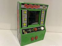 Front three-quarter view of the green vintage Frogger tabletop game showing screen, joystick, buttons, and side artwork.
