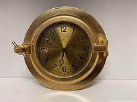 Front view of vintage brass ship clock showing brass tone clock face with black numerals and hands.