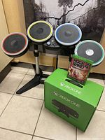 Rock Band drum set with four colored pads, foot pedal, Xbox One original console box, and Rock Band 4 game disc case.