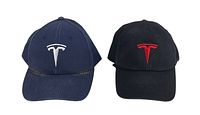 Front view showing navy blue and black Tesla strap back hats with respective white and red embroidered Tesla logos.