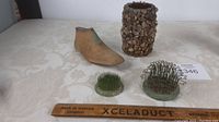 Antique wooden shoe last, two cast and wire flower frogs, and a vase covered with small stones arranged on a table with a ruler for scale.