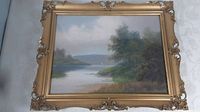 Full view of the antique framed oil painting showing a river landscape with trees and a sailboat under a cloudy sky.