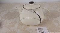 Front and side view of Denby Oyster Strands teapot showing the cream body with black swirl design, round lid with black knob, handle and spout.