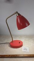 Red desk lamp on a table with neutral background, showing the lamp illuminating in the second photo, and different angle views in all photos.