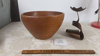 Side view of teak wooden salad bowl next to twisted metal candle stand with a ruler for size reference.