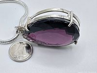 Side view of large pear-shaped amethyst pendant showing depth and setting with coin for size reference