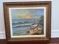 Framed artwork showing beach scene with waves, boats, and people under soft sunset sky.
