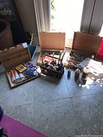 Three open wooden artist boxes and basket on tiled floor under natural light.