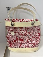 Front view of Burberry purse showing clear plastic body, white leather top trim embossed with 'BURBERRY', and red and white floral fabric bag insert with charm attached.