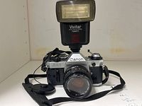 Front view of Canon AE-1 with lens, flash, strap and lens cap