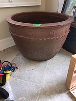 Side view of large terracotta ceramic pot showing floral relief band and scalloped rim.