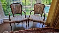 Pair of vintage carved wood armchairs with fabric upholstery, placed in front of a large window.