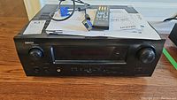 Front view of Denon AVR-1610 AV surround receiver showing power and control knobs, front digital display, and various input/output ports.