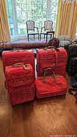 Front view of all four red and white DVF luggage pieces arranged on wooden floor.