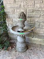 Full view of three-tier fountain with pump against stone wall