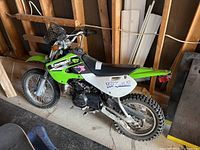 Full left side view of Kawasaki KLX 110 dirt bike showing green plastic fenders, black seat, silver frame and knobby tires