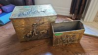 Two vintage hammered metal wood boxes with detailed hunting scenes in bas relief placed on wood floor