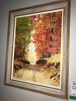 Framed fall landscape painting featuring a dirt road flanked by trees with green and red-orange leaves, signed H Lipscombe, showing overall view including frame.