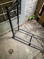 Partial front view of one end of the black metal firewood rack showing decorative scroll side panel and frame.