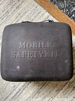 Black rectangular nylon zipped case with a handle, embossed with text "MOBILE SAFETY KIT" on surface.