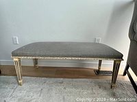 Front view of fabric covered bench showing rectangular cushion and carved, hand-painted legs with vertical grooves and light cream paint.