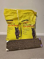 Two yellow 10 kg bags of generic unscented cat litter with a black cat image on the front alongside a rectangular cardboard cat scratcher.