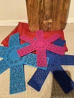Set of three felt cookware protectors in blue, pink, and navy on floor with wooden cutting board leaning against wall and red tablecloth under them