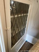 Front view of one white painted cabinet door with diamond-shaped glass grid, installed inside a cabinet opening, showing warped glass.