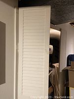 Full view photo of the two old-fashioned white panel doors standing upright indoors, showing height and slatted panel design.