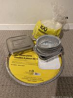 Overview of Lunchbots metal tin, 2 large aluminum pizza pans, mixed foil pans and paper plates in yellow packaging.