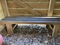 Wide angle view of wooden bench inside outdoor wooden playhouse, low to the ground on wood chip and leaf floor.