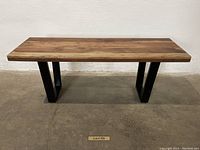 Front view of a hardwood bench with thick natural wood grain top and black steel legs.