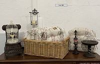 Wide shot showing the full lot of country French style items including cushions, wicker chair, basket, candle holder, birdcage, and glass dome.