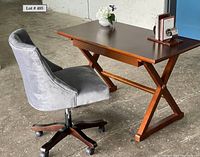Side view of wooden desk, blue upholstered swivel chair on casters, Mid-Century Modern style book holder, and vase with faux flowers placed on desk.