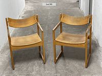 Front view of two matching mid-century modern wooden chairs with sling backs showing minimal wear.