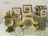 Full overview of lot items arrayed on table showing framed artwork, candles, ceramic bowl, baskets, fabric placemats, flowers, decorative pears and assorted smaller items