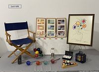 Full lot view showing wooden director's chair, framed Picasso print, three modern art triptych pieces, pool balls, bocce balls, rainbow domino sets, rainbow martini glasses, aqua globes, stamper pads, and gum ball machine.