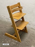 Front view of the Stokke Tripp Trapp child's high stool showing adjustable wooden seat and footrest, angled frame, and black support rods.