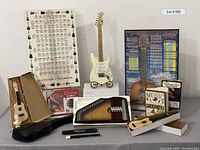 Wide shot showing all included items: small white electric guitar on stand, two guitar posters behind, two ukeleles in boxes, Autoharp ChromAharp in box, music encyclopedia, Simply Guitar book and DVD, recorder, guitar case and tuners spread out on table.