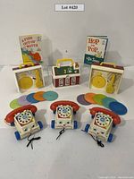 Photo showing three Fisher-Price rotary dial toy telephones with attached cords, two vintage Fisher-Price record players and plastic records, two Dr. Seuss books, and a schoolhouse lunchbox.
