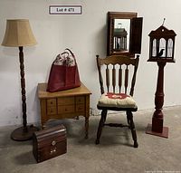 Full view of the lot showing the floor lamp, end table with red carryall bag on top, solid wood chair with cushion, small wooden trunk, and bird cage on newel post with wall mirror behind.