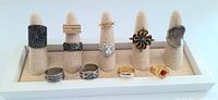 Eleven vintage cocktail rings arranged on ring display cones, showing variety of styles in silver and gold tones with stones and filigree designs.