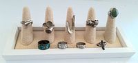 Twelve vintage sterling silver rings arranged on beige fabric ring holders on a white tray. Various styles including gemstone and textured silver bands.