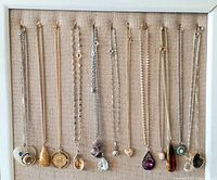 All 15 vintage necklaces with pendants including natural stones and various metal types, displayed on a fabric background showing chain styles and pendant shapes.