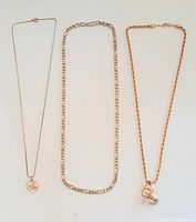Three gold necklaces laid flat on white background showing overall visual and different pendant styles.