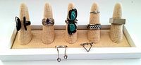 Seven sterling silver rings displayed on fabric finger stands, showing diverse styles including turquoise stones, amethyst, patterned bands, and simple bands.