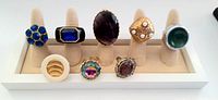 Eight vintage cocktail rings displayed on ring holder, showing each ring's size, stone color, and design details.
