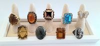 Front view of nine distinct vintage cocktail rings on ring holders showing various colored stones and designs.