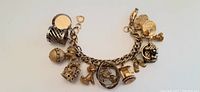 Gold-tone chunky link charm bracelet with 9 diverse charms including a locket, birdcage, acorn, crown, dog, rose, letter H, ball, and coin charm shown in full view
